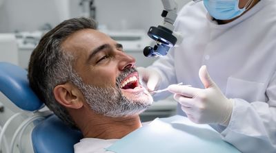 Mexican dentist cementing zirconia bridge into American patient’s mouth under bright LED lights