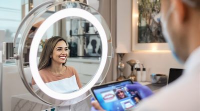 Happy patient admiring final denture results with dentist showing before and after progression photos.