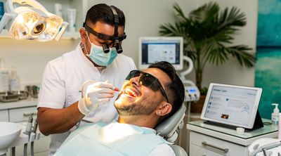 A Mexican dentist bonds final veneers to a diverse male patient's teeth, revealing a natural smile.